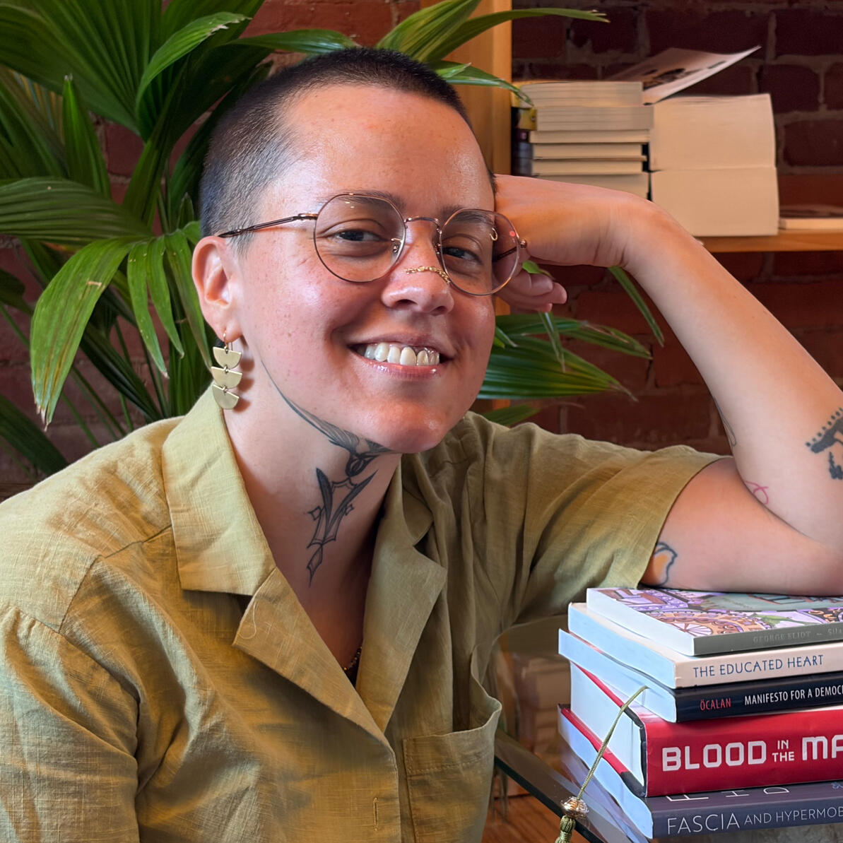 Nellie Grant, LMT A photo of Nellie Grant, the owner and sole practitioner at Cloudbelly Bodywork LLC. The photo shows their smiling face turned toward the camera with warmth and comfort in their brown eyes. They are wearing wire-framed glasses, dangly earrings, and a their